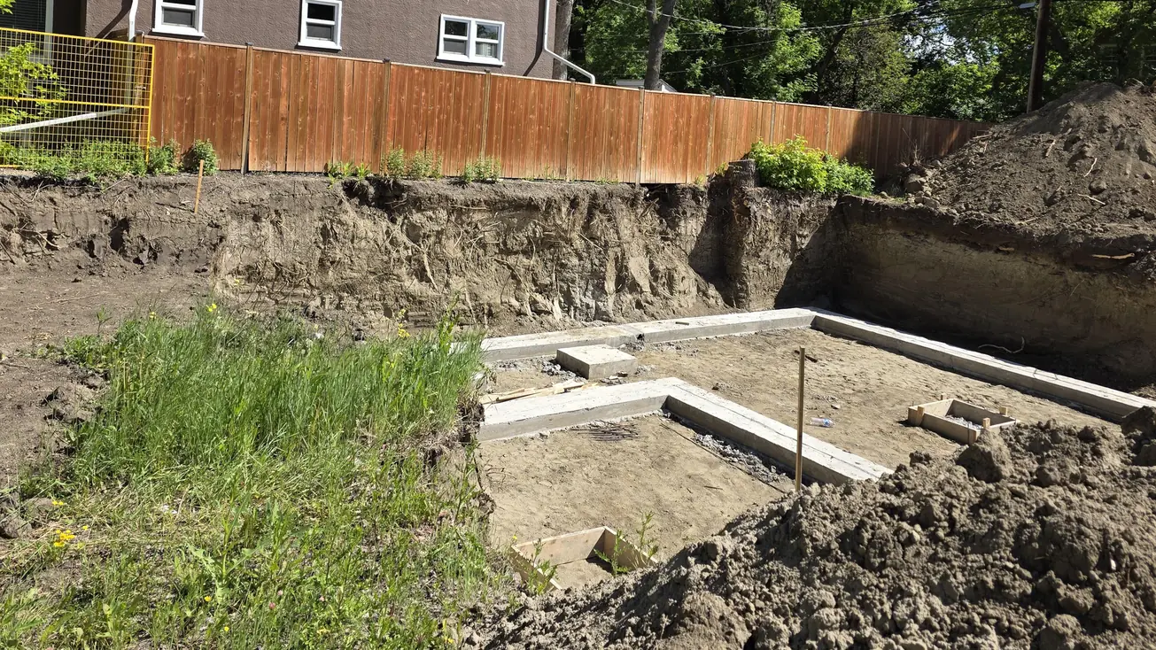 Excavated foundation cut with poured footings set out and spoil piled along the bank