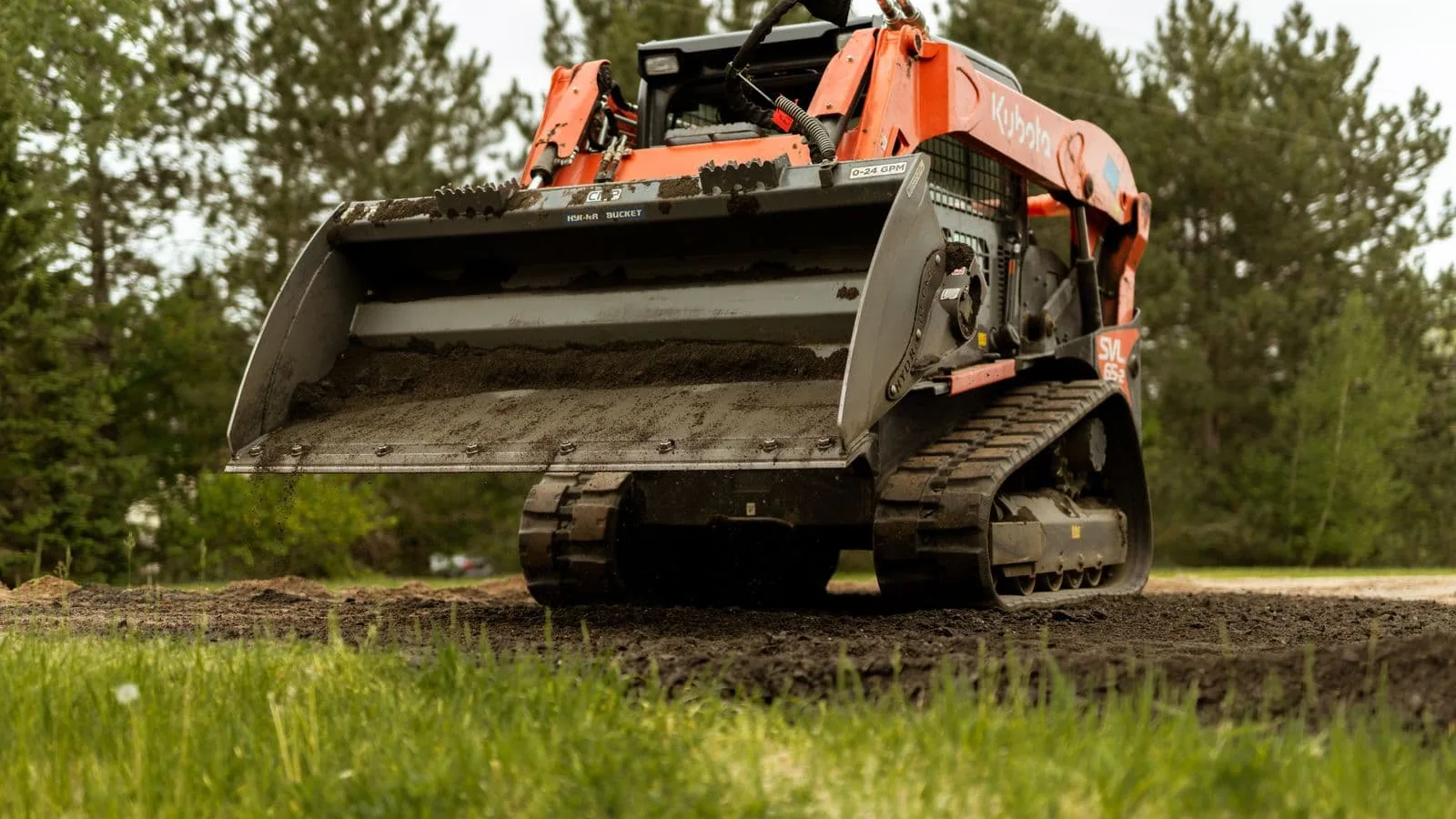 Compact track loader carrying a full bucket of dirt across a job site