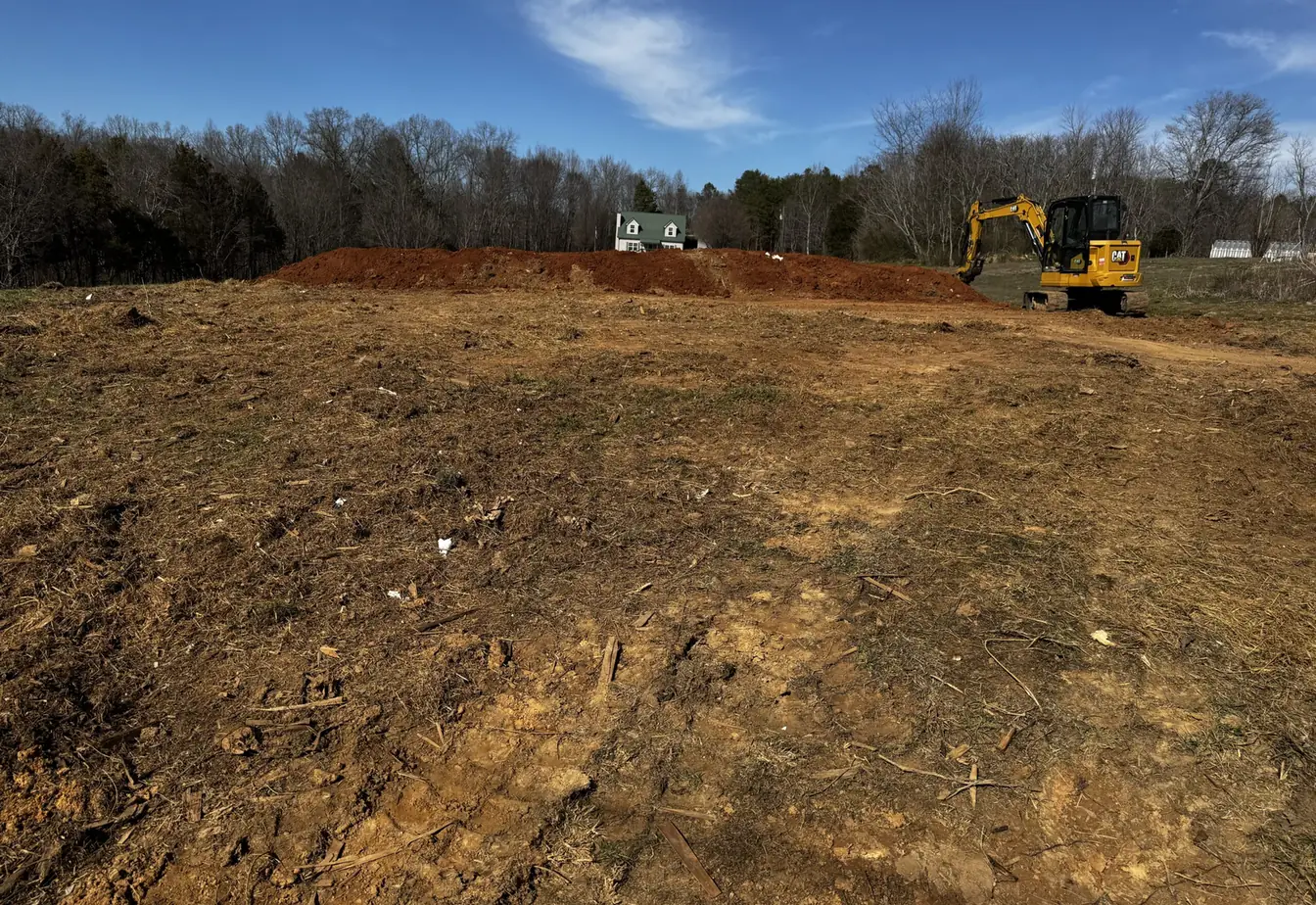 Tracked excavator on a cleared building site with a long berm of excavated dirt