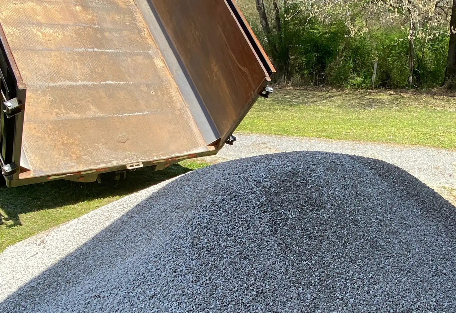 Dump bed raised over a fresh pile of grey gravel on a north Louisiana driveway